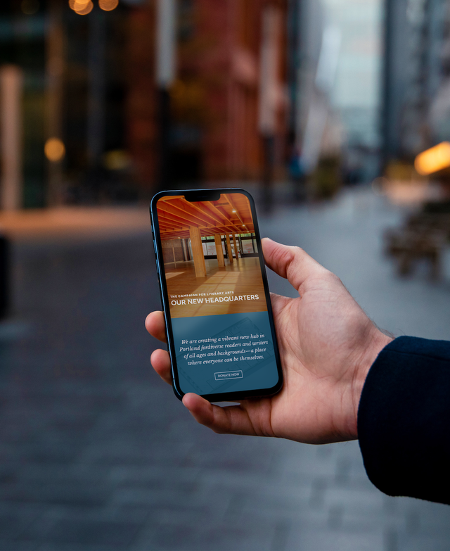 Hand holding an iPhone that shows the Our New Headquarters page on the Literary Arts website showcasing an interior view of the open space