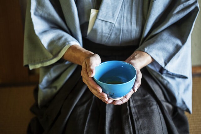 Man holding blue tea bowl during tea ceremony.